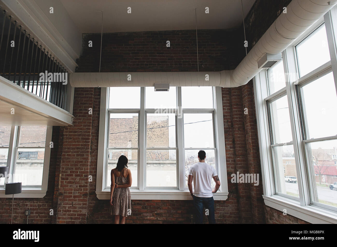 Brunette man and woman standing looking out of city loft Appartement Banque D'Images