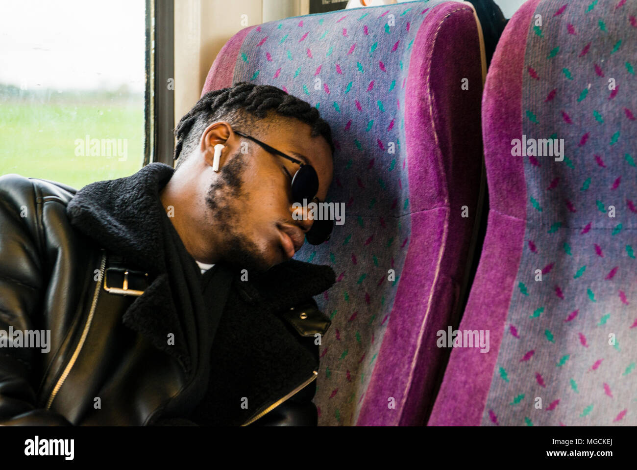 Jeune homme portant des lunettes de soleil, assis sur le train, dormir Banque D'Images