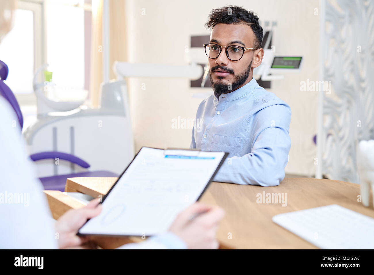 Femme dentiste wearing white coat assis à un bureau et remplissant medical record tout en consultant les young patient Banque D'Images