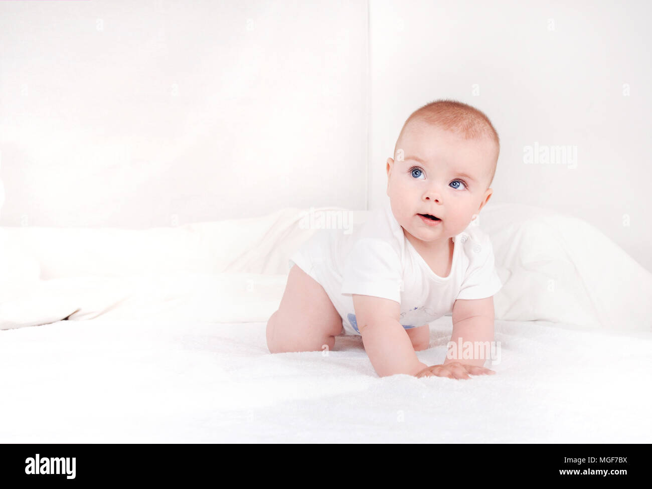Portrait de nouveau-né doux sur crawlng grave de lit blanc à la route. Happy smiling enfant aux yeux bleus sur fond de lit blanc Banque D'Images