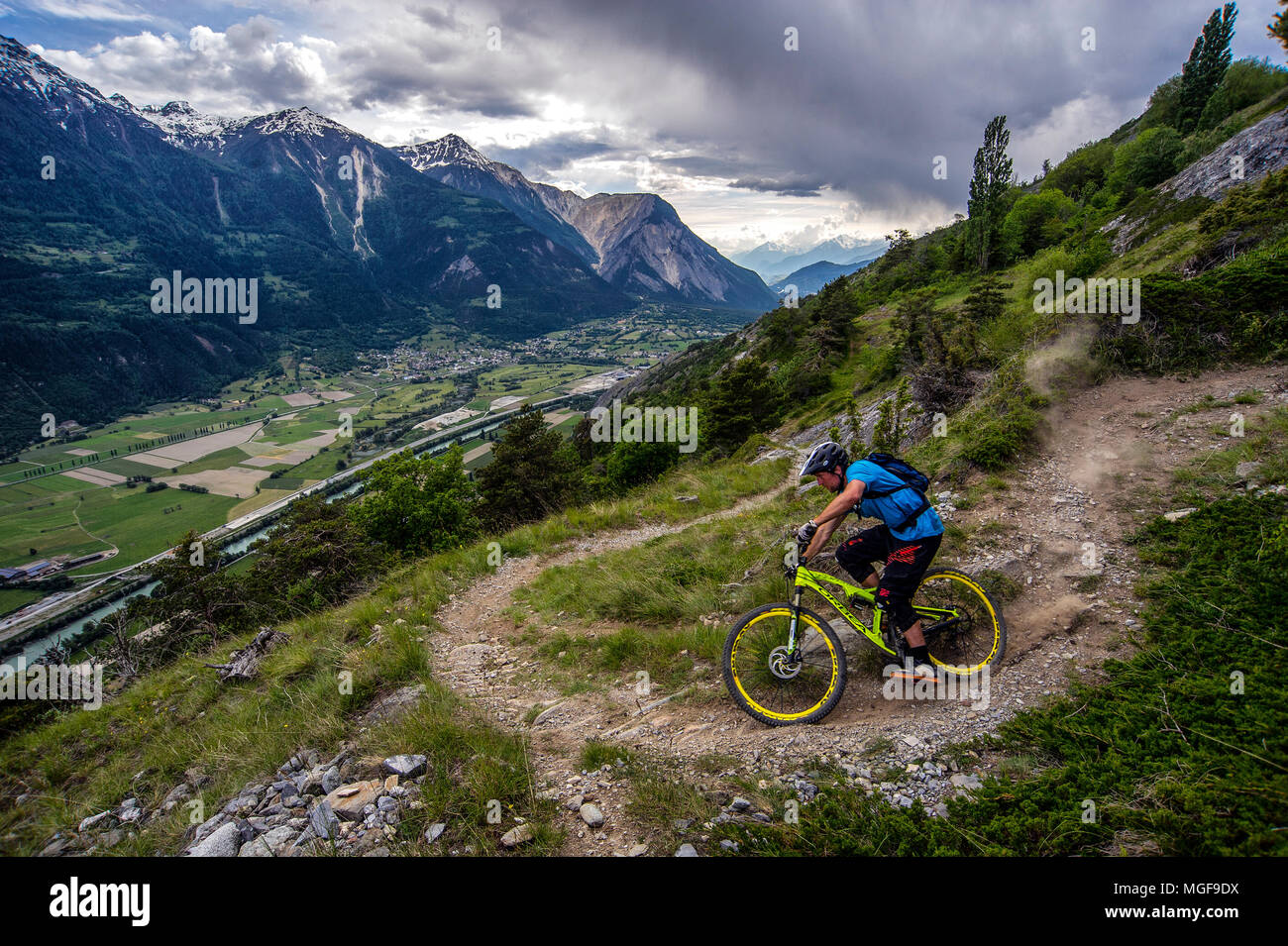Un homme monte un vtt haut au-dessus de la vallée, près des villes de Gampel et Jeizinen dans le Valais Suisse. Banque D'Images