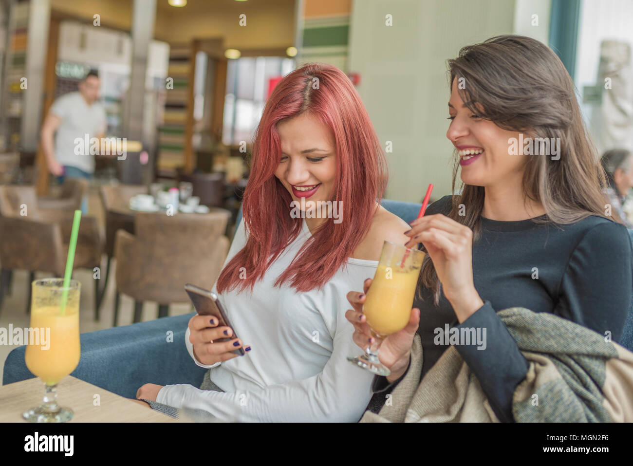 Portrait de deux jeunes belles femmes à l'aide de téléphone mobile au coffee shop. Deux jeunes femmes bénéficiant d'amis ensemble dans un restaurant de rire, parler Banque D'Images