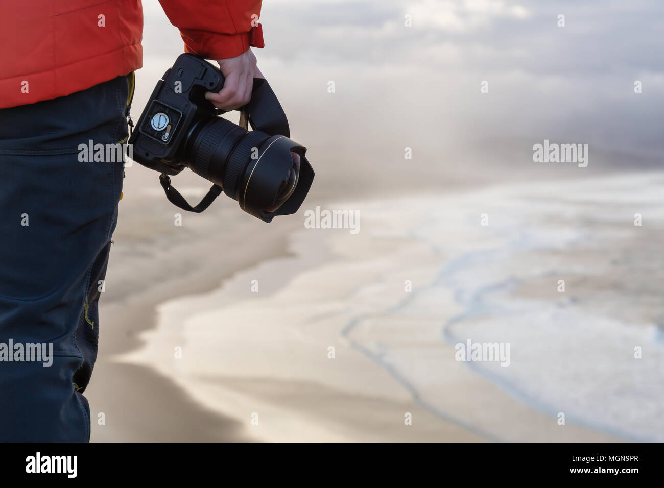 Homme tenant un appareil photo à la main donnant sur la belle plage de sable au cours d'un hiver dynamique le lever du soleil. Prises à Cape Kiwanda, Pacific City, Oregon Co Banque D'Images