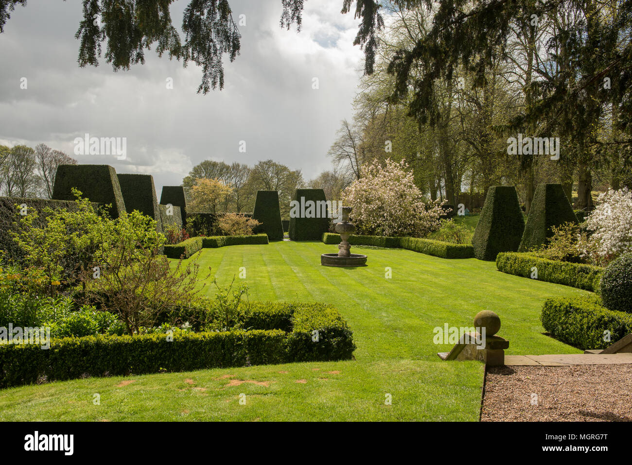 Jardin anglais formel avec topiaire, pelouse bien entretenue et fleurs printanières sous un ciel spectaculaire dans un cadre historique. Banque D'Images