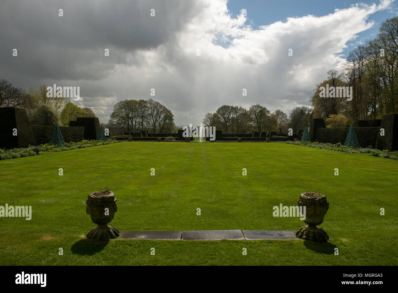 Jardin anglais formel avec topiaire, pelouse bien entretenue et fleurs printanières sous un ciel spectaculaire dans un cadre historique. Banque D'Images