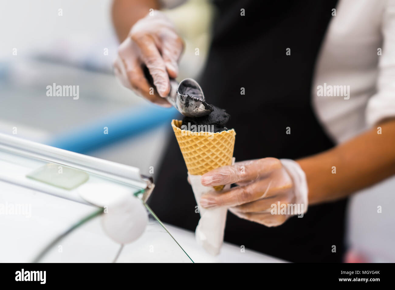 Beau jeune garçon en costume classique élégant noir boules de crème glace mettant en cornet gaufré. Dessert à la mode. Scène réelle. Service professionnel, restauration Banque D'Images