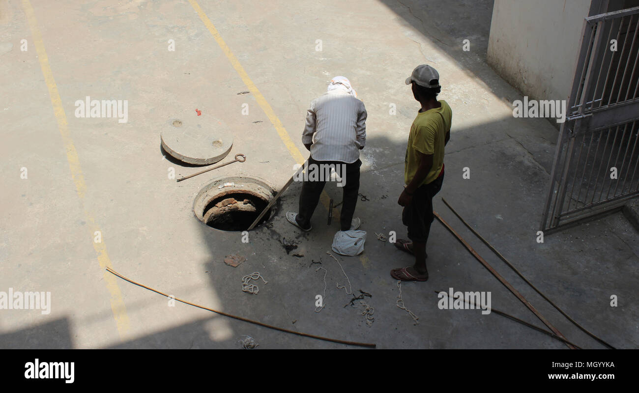 Nettoyage d'un trou d'homme indien de Delhi sur une chaude journée d'été couvrant la tête et le visage avec un chiffon. Son assistant est debout à proximité portant une casquette. Banque D'Images