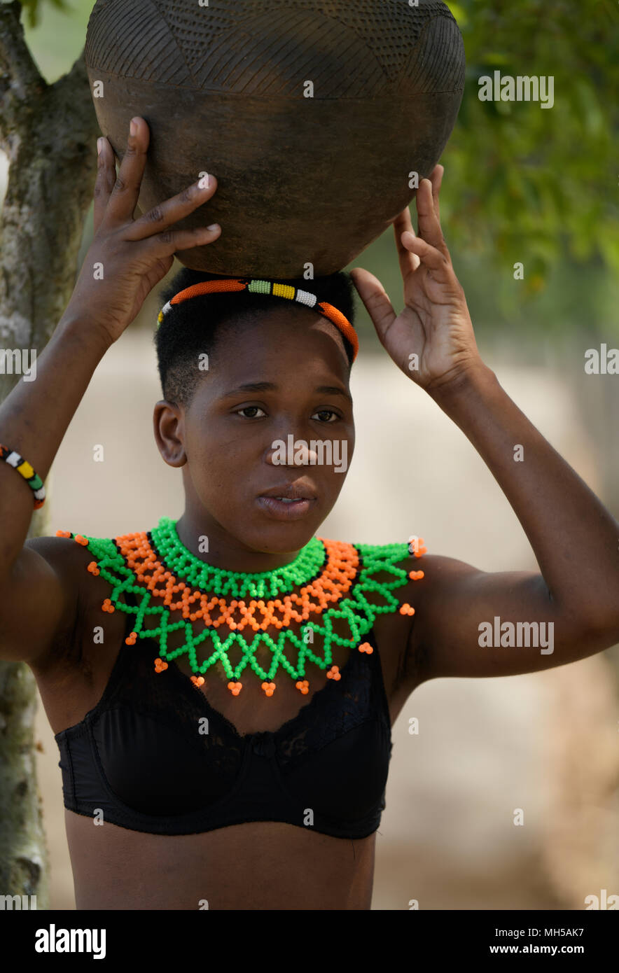 Eshowe, KwaZulu-Natal, Afrique du Sud, seule jeune femme, robe perlée traditionnelle zouloue, exerçant son pot en argile sur la tête, visage, village thème Shakaland Banque D'Images