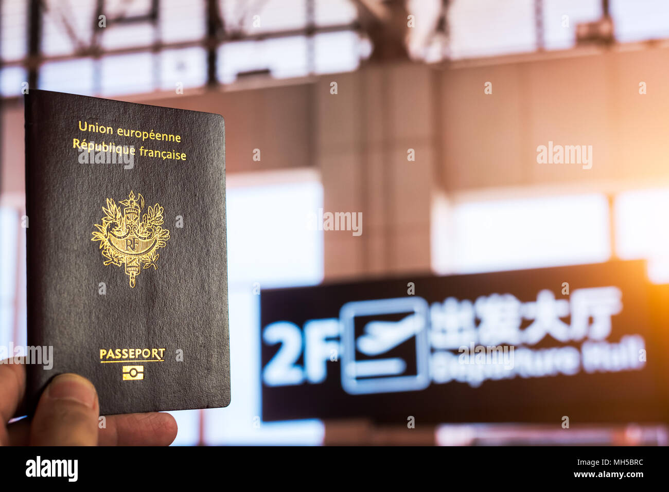 Main tenant un passeport français dans un hall de départ de l'aéroport chinois avec le soleil passant à travers les fenêtres Banque D'Images