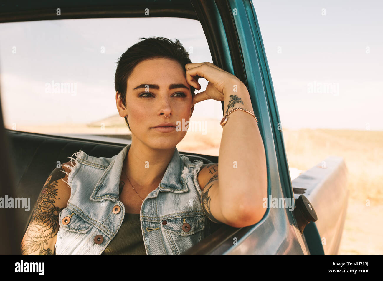 Femme sur un voyage sur la route dans une voiture. Femme avec des tatouages sur les bras à la sortie de sa voiture assis à la fenêtre. Banque D'Images