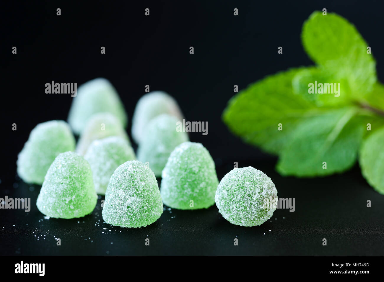 Close up of green, gelée de menthe avec gouttes de cristaux de sucre et de feuilles de menthe douce sur un fond noir Banque D'Images