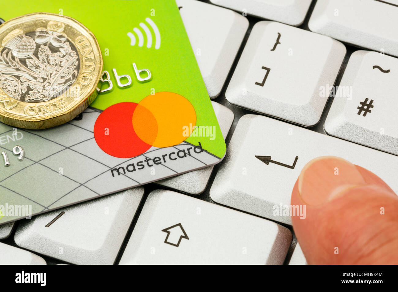 La Lloyds Bank Mastercard carte de crédit sans contact et d'une livre pièce sur un clavier avec un doigt qui appuie sur la touche entrée. Concept d'achat en ligne. UK Banque D'Images