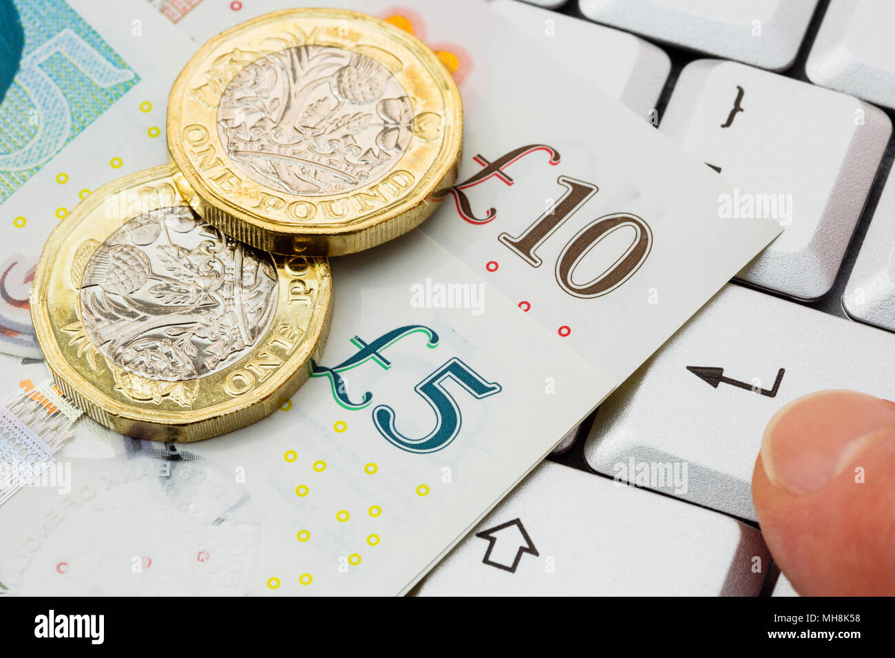 Livres sterling £5 et £10 livres de billets avec de nouvelles pièces de livre livres livres livres sur un clavier avec un doigt d'une personne en appuyant sur la touche entrée pour acheter le concept d'achat en ligne. ROYAUME-UNI Banque D'Images
