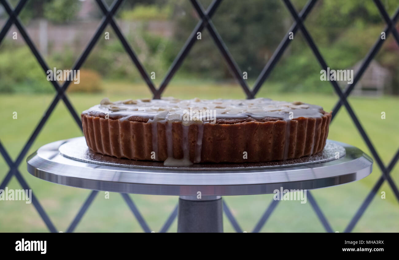 Tarte Bakewell cake faits maison sur metal cake stand en face de la fenêtre, avec vue sur le jardin derrière. Banque D'Images