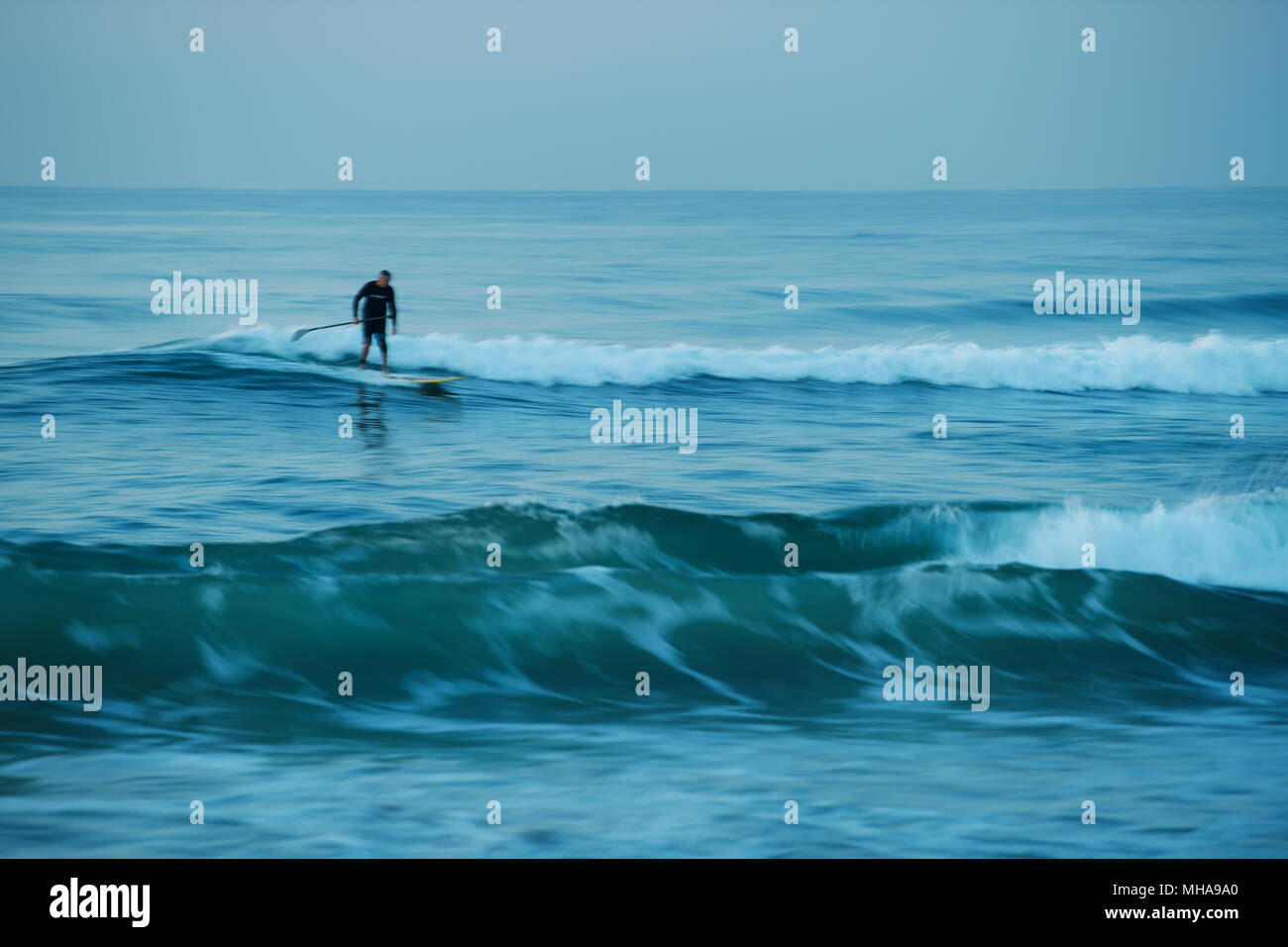 Durban, le KwaZulu-Natal, Afrique du Sud, flou de mouvement, homme adulte surf une vague sur stand up paddle board, plage d'Umhlanga Rocks Banque D'Images