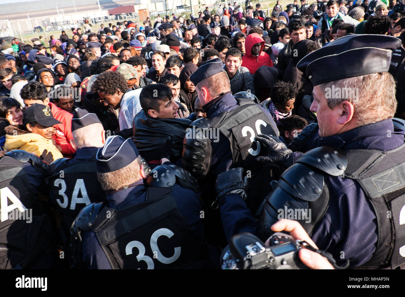 Les réfugiés et les migrants à résister à la ligne de la police au cours de l'évacuation de la jungle. La police française a retiré le jeune homme à l'origine des problèmes dans la foule. La Jungle était un camp de migrants dans le nord de la ville française de Calais. Le camp attiré des migrants et des réfugiés du Moyen Orient, Afrique du Nord et l'Afrique subsaharienne qui ont planifié d'entrer illégalement au Royaume-Uni. Finalement, les autorités françaises ont été obligés de fermer la Jungle parce qu'il était devenu hors de contrôle et devient à la fois un risque pour la santé publique et un centre d'activité criminelle. La Jungle de Calais a été fermé en octobre Banque D'Images