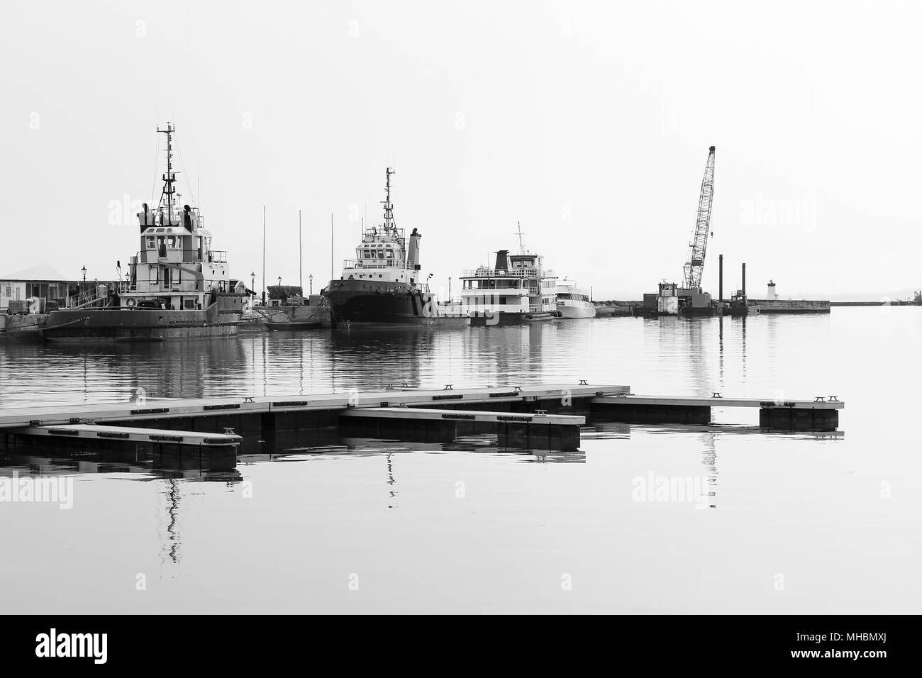 Une flotte de bateaux-pilotes contre un mur du port, sur une journée brumeuse, en noir et blanc Banque D'Images