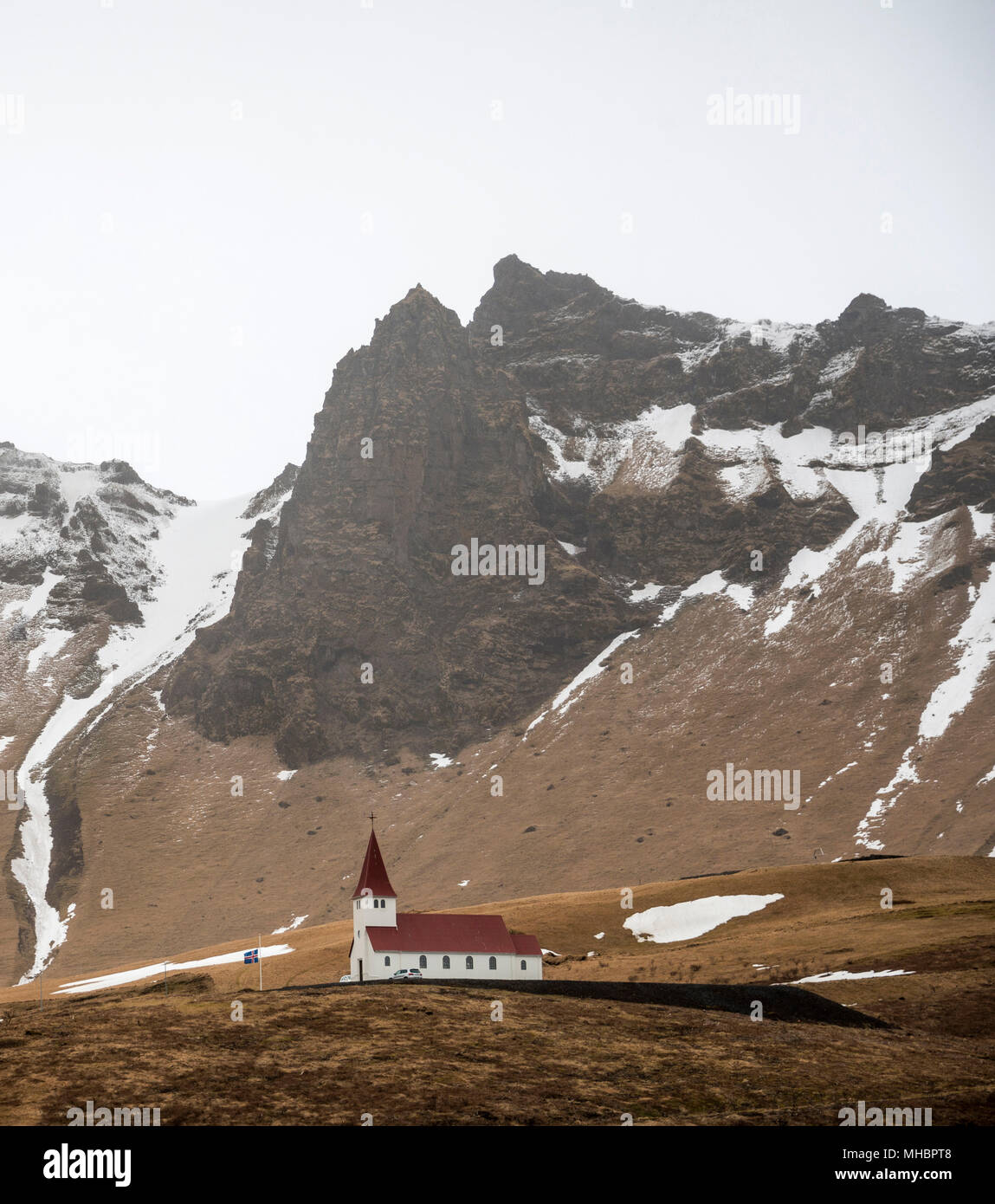 Rouge Blanc église, Víkurkirkja en face de montagnes enneigées, Vík í Mýrdal, côte sud, Islande Banque D'Images