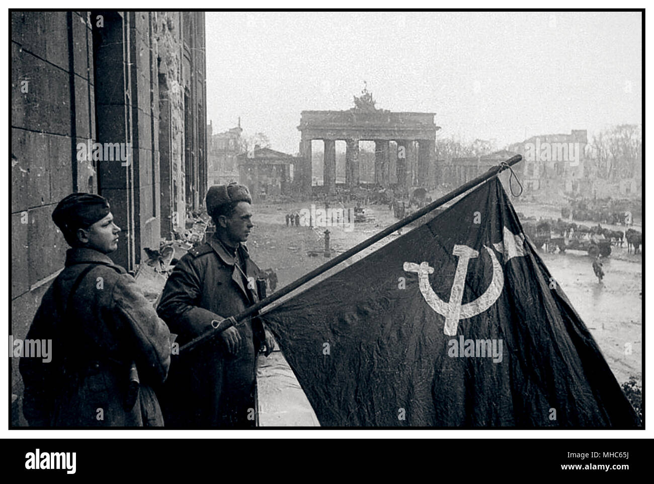 1945 les soldats russes de la Seconde Guerre mondiale tiennent fièrement leur symbole national le drapeau du marteau et de la faucille dans la victoire Berlin Allemagne la porte de Brandebourg se trouve dans un état très piqué et meurtris. Autrefois symbole de la fierté allemande, ici en mai 1945, il se trouve presque en ruines Banque D'Images