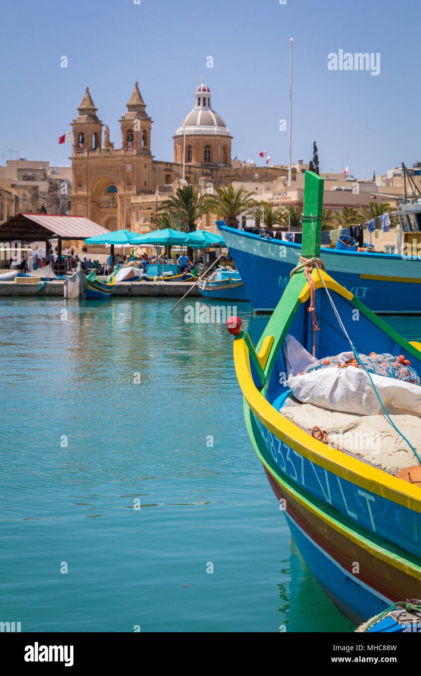 Luzzu maltais colorés traditionnels bateaux de pêche dans les eaux bleu turquoise de Marsaxlokk Harbour, avec la belle église paroissiale de Notre-Dame de P Banque D'Images