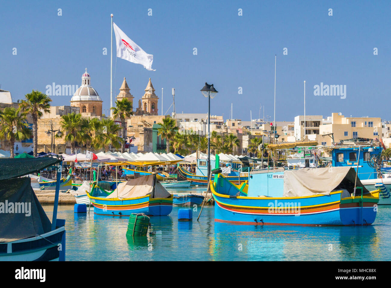 Luzzu maltais colorés traditionnels bateaux de pêche dans les eaux bleu turquoise de Marsaxlokk Harbour, avec la belle église paroissiale de Notre-Dame de P Banque D'Images