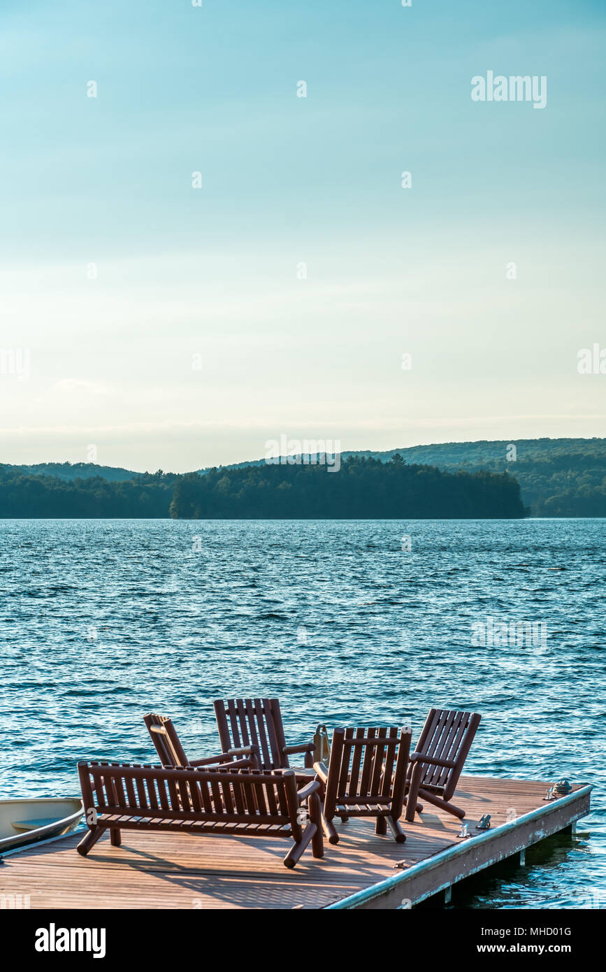 Un bateau à côté d'un quai, avec des chaises en bois, comme la fin de l'été soleil se couche. Banque D'Images