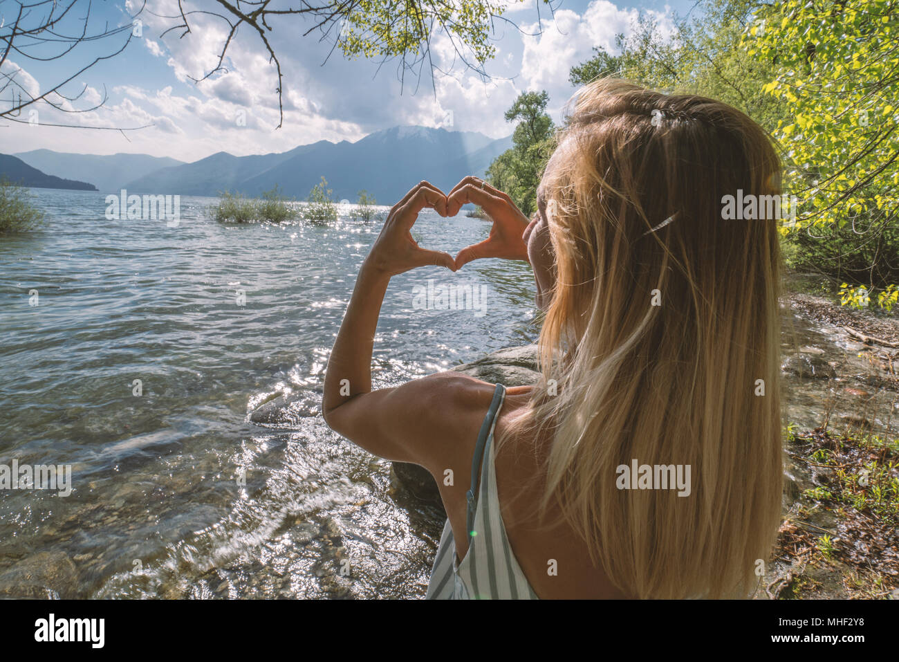 Jeune femme au bord du lac en forme de coeur fait avec les mains de paysage de montagne, tourné dans le Canton du Tessin, Suisse, Europe. Les gens de l'environnement voyage Banque D'Images