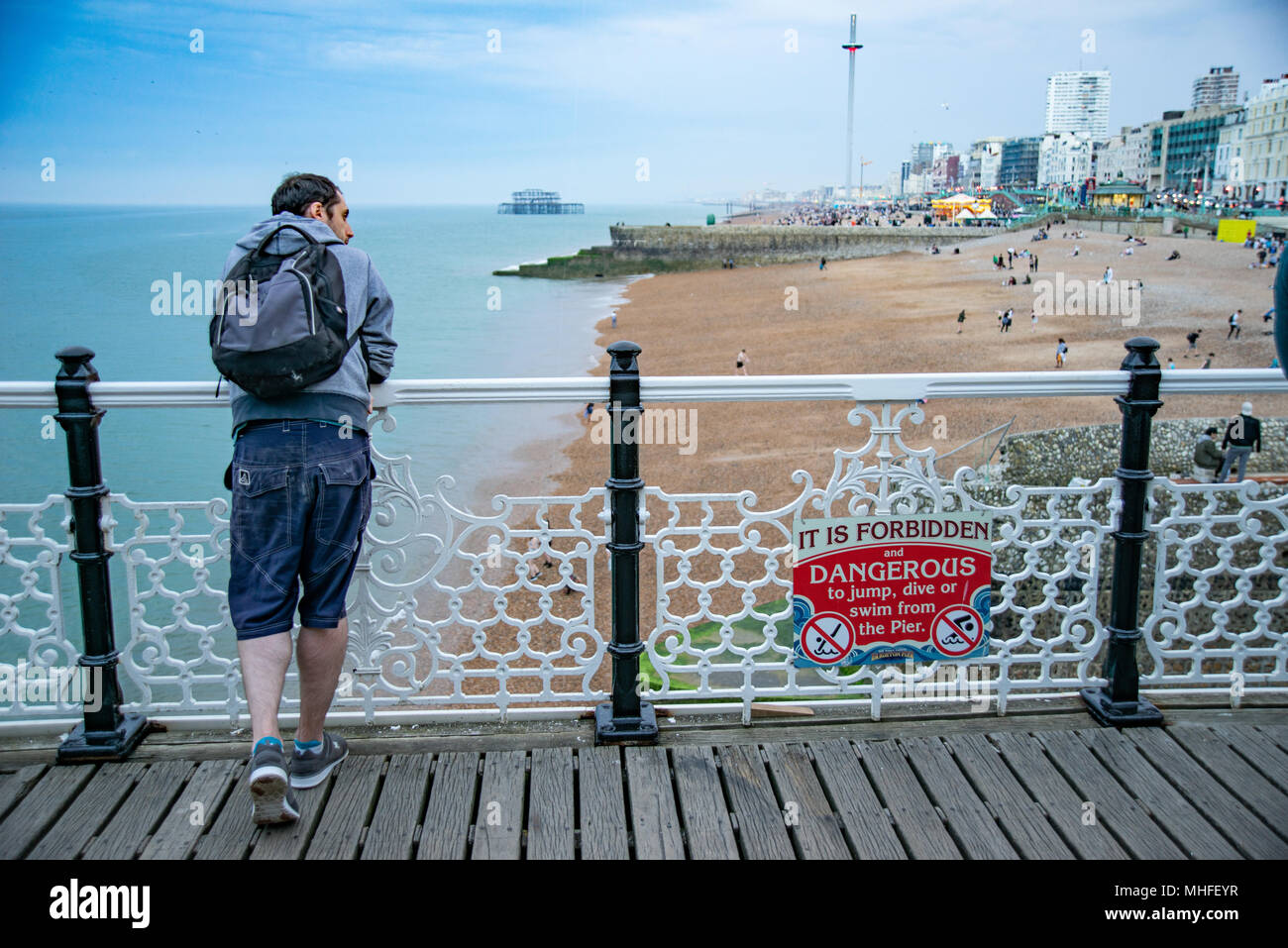 Adultes mâles figure seul sur la jetée de Brighton par voir les gens sur la plage Banque D'Images