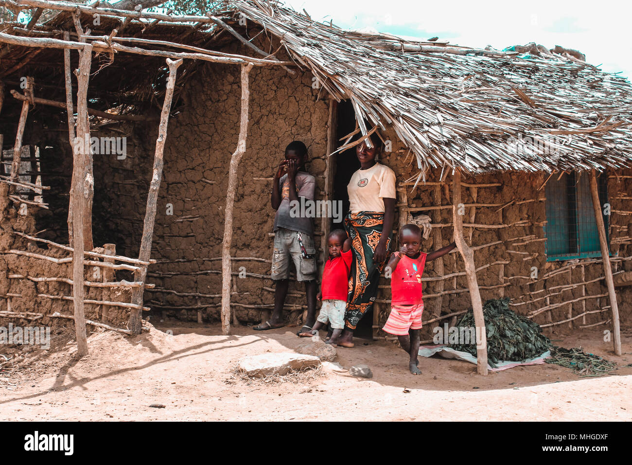 Une famille pauvre d'Afrique composé de trois enfants et leur mère, mettre hors de leur hutte faite d'excréments et de ciment sur les frontières de la Savane Banque D'Images