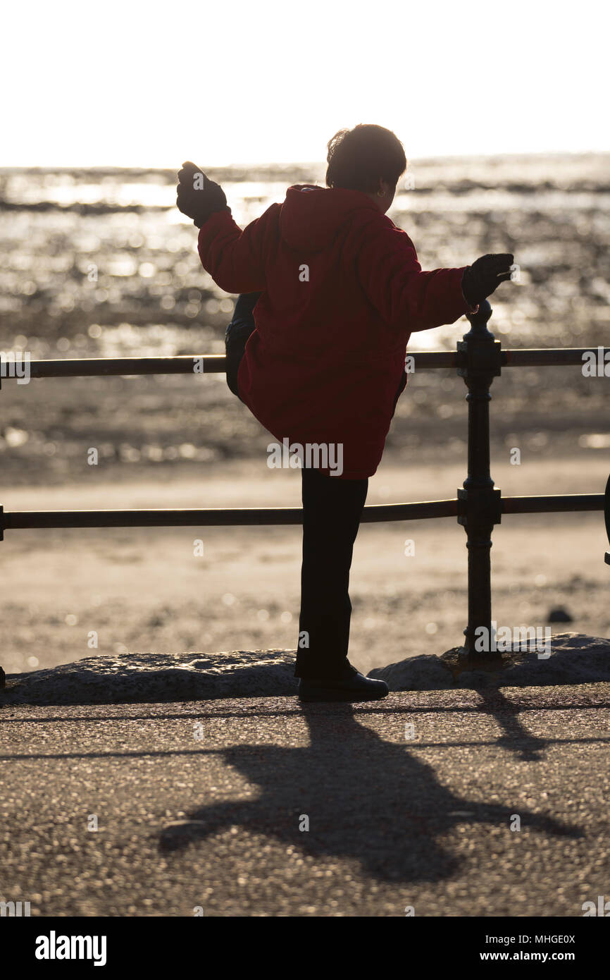 Une vieille femme chinoise faire tôt le matin, l'exercice de tai chi en utilisant les rampes sur la promenade du bord de mer pour l'appui à Llandudno, au Pays de Galles Banque D'Images