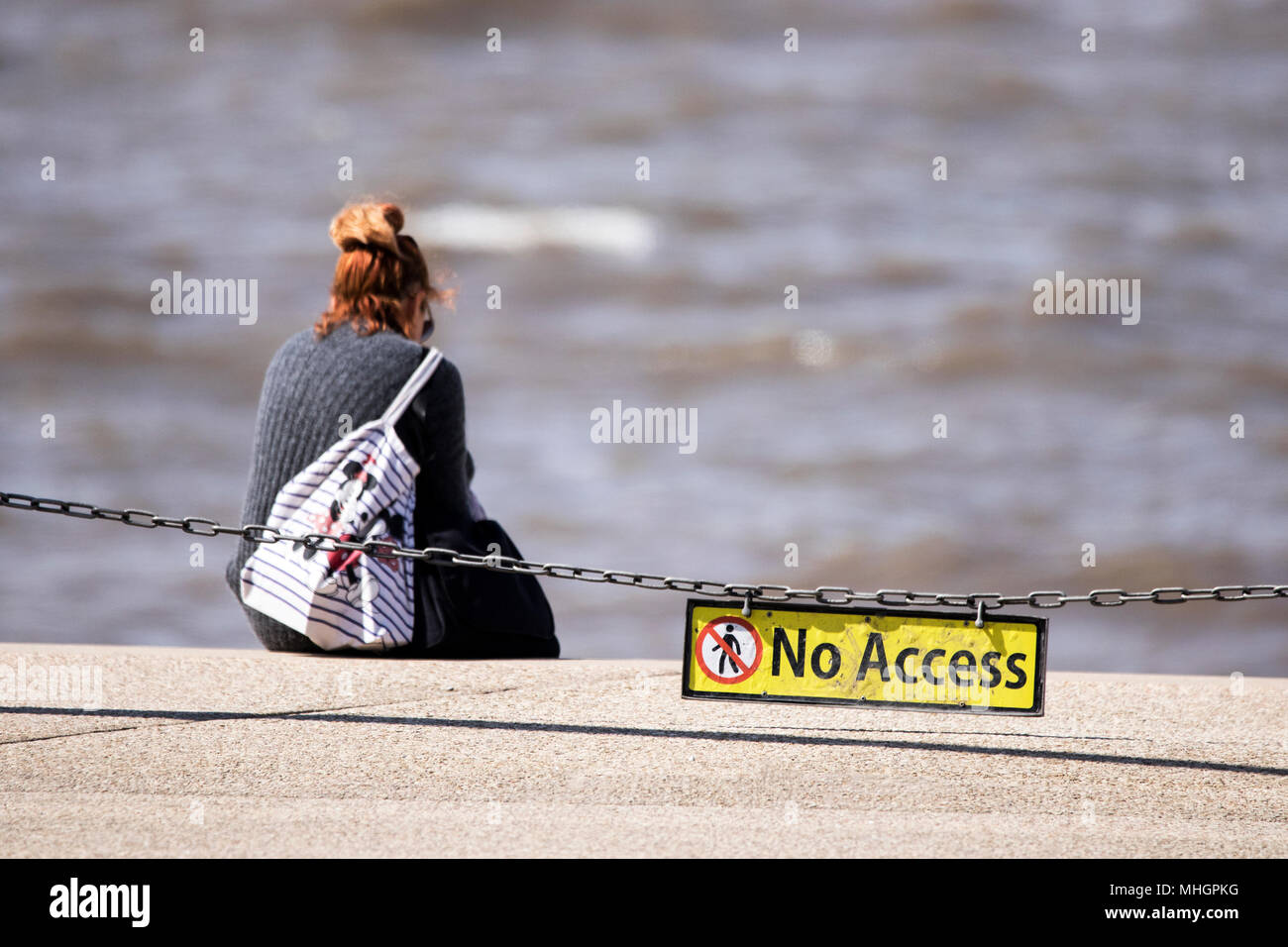 Une femme seule se trouve l'regarder la marée monter à bord de mer de Blackpool, derrière une chaîne de sécurité d'accès dans le Lancashire, Royaume-Uni. Banque D'Images