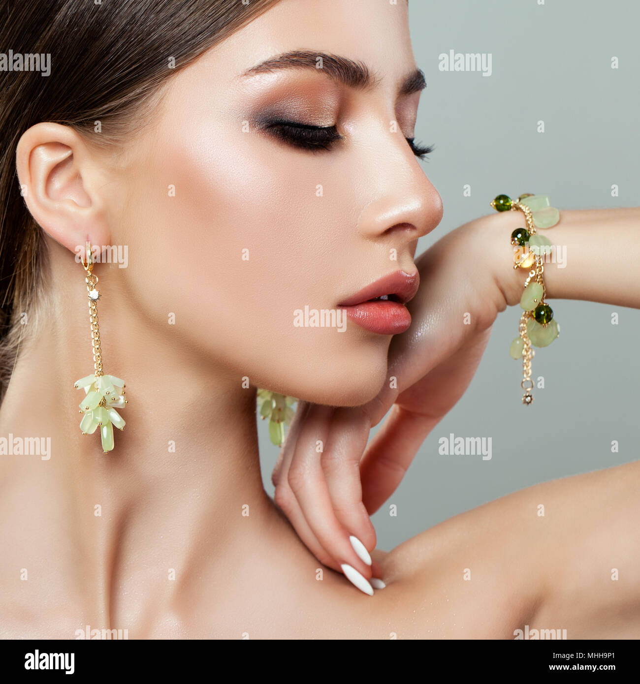 Belle femme Face Closeup Portrait. Jeune modèle féminin parfait visage avec le maquillage, bracelet et boucles d'or avec Perle Verte Banque D'Images