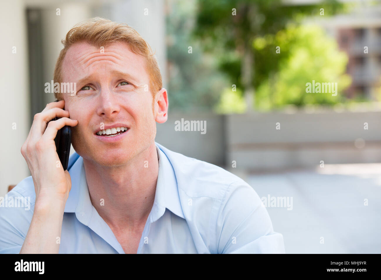 Closeup portrait, inquiets à l'jeune homme en chemise bleue parlant au téléphone à quelqu'un, à la sombre, isolé à l'extérieur hors contexte Banque D'Images