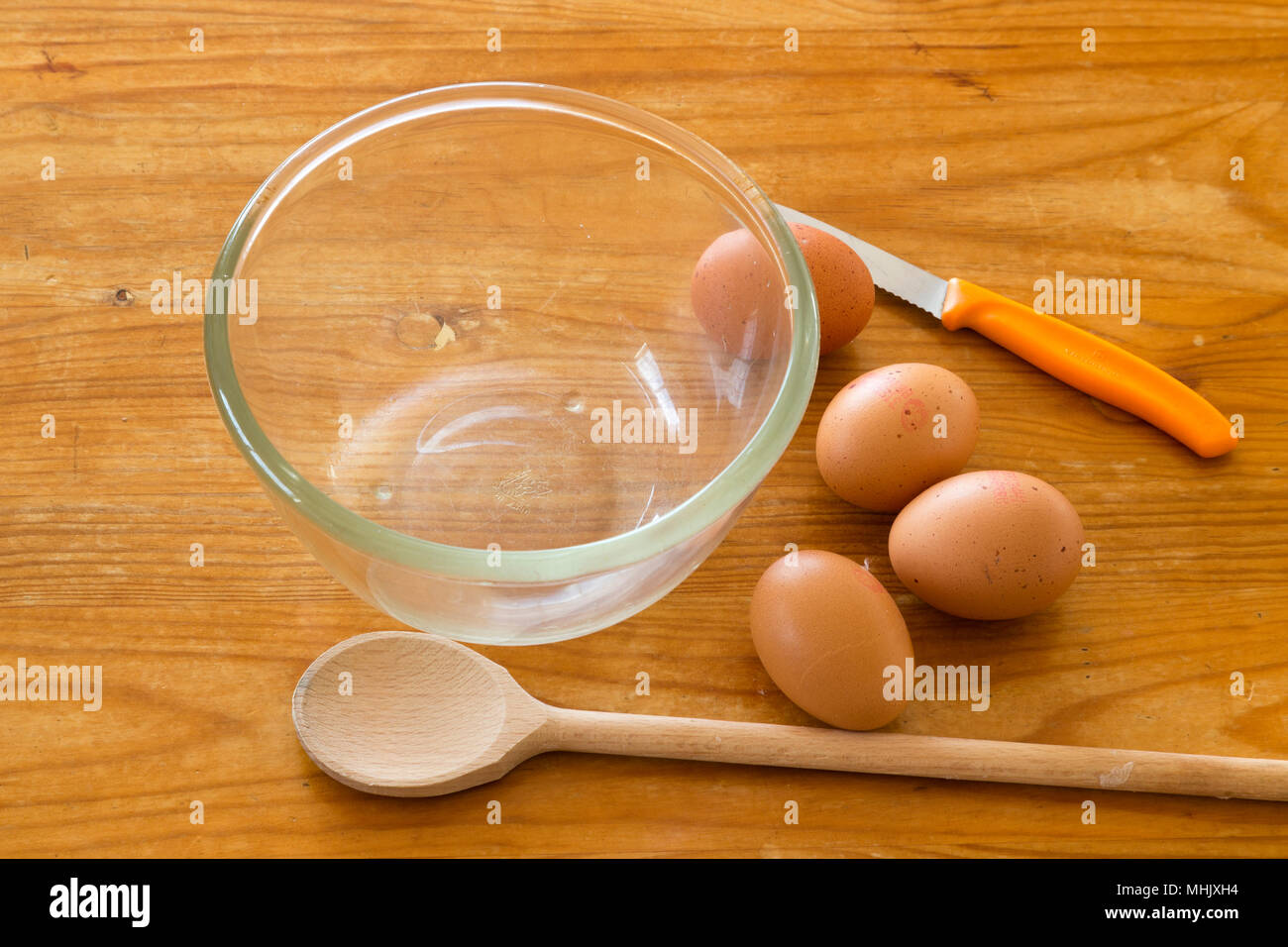 Les œufs, cuillère en bois, un couteau et bol en verre sur une table à faire des œufs brouillés Banque D'Images