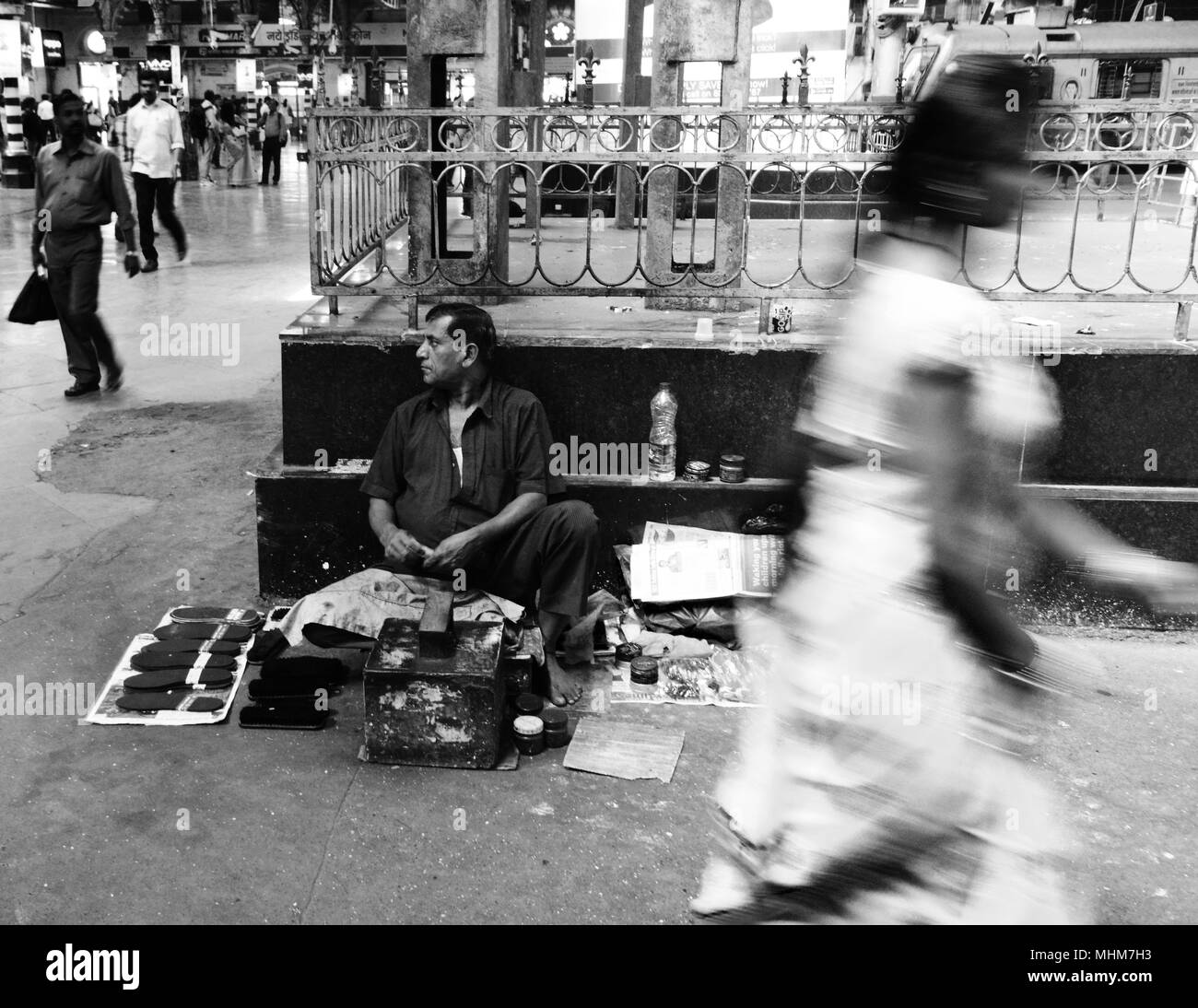 Un cordonnier assis à regarder passer les navetteurs dans le grand hall dans le TCPS, Mumbai, Inde Banque D'Images