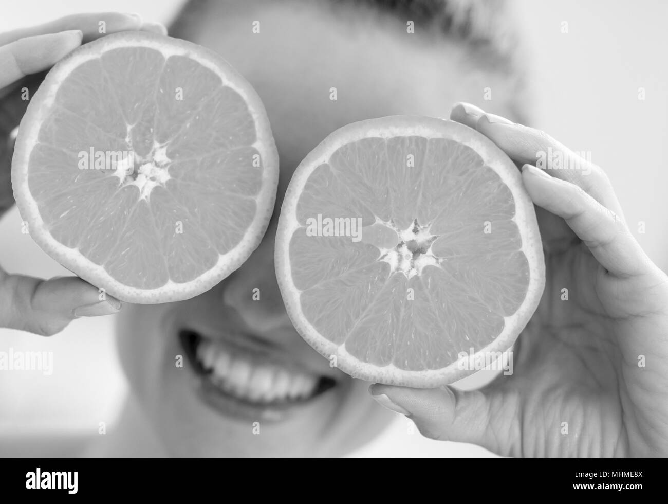 Happy young woman holding deux tranches d'orange en face des yeux Banque D'Images
