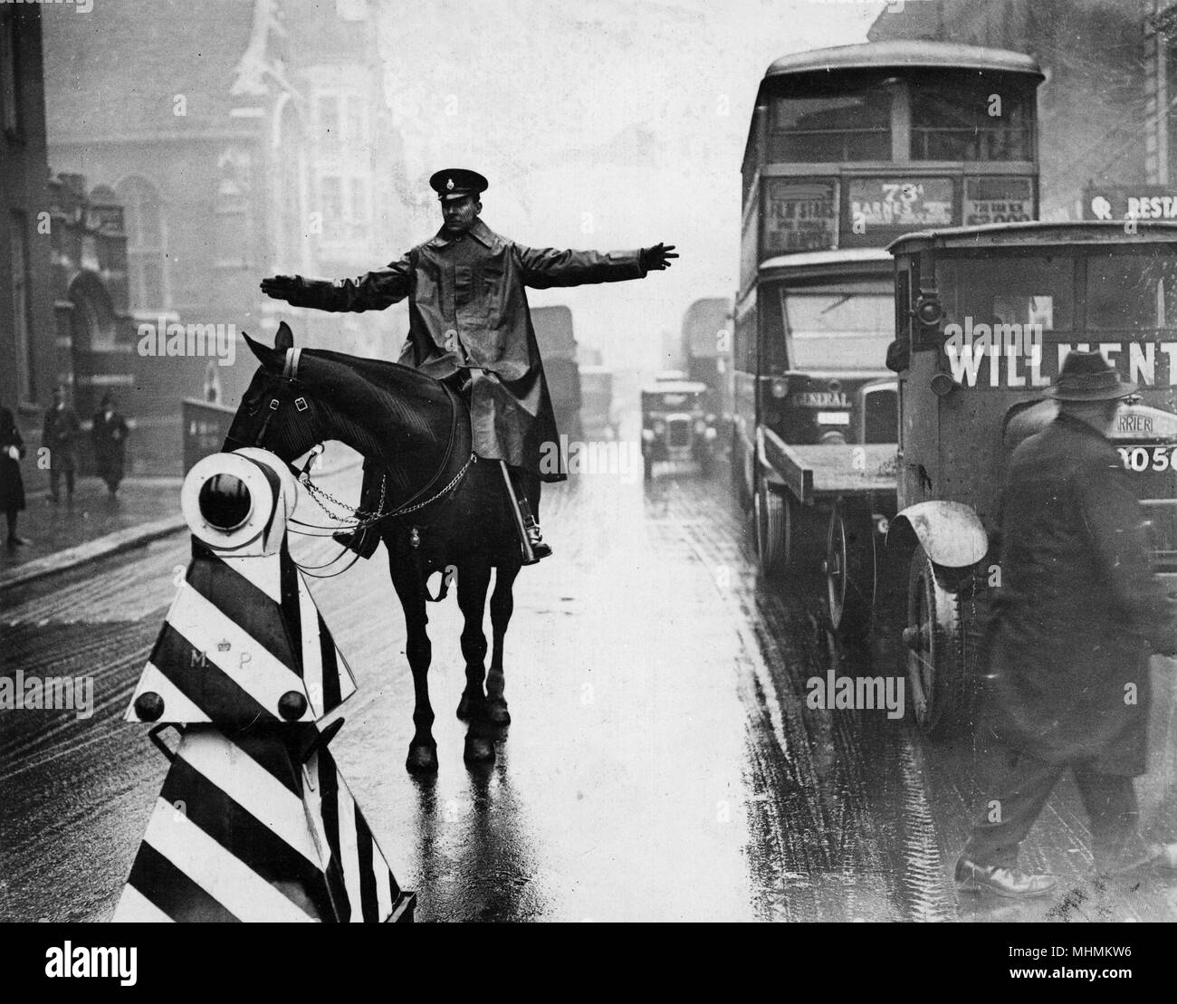 Un policier à cheval dirige le trafic de Londres et permet aux piétons de traverser la route sous la pluie battante. Date : 1931 Banque D'Images