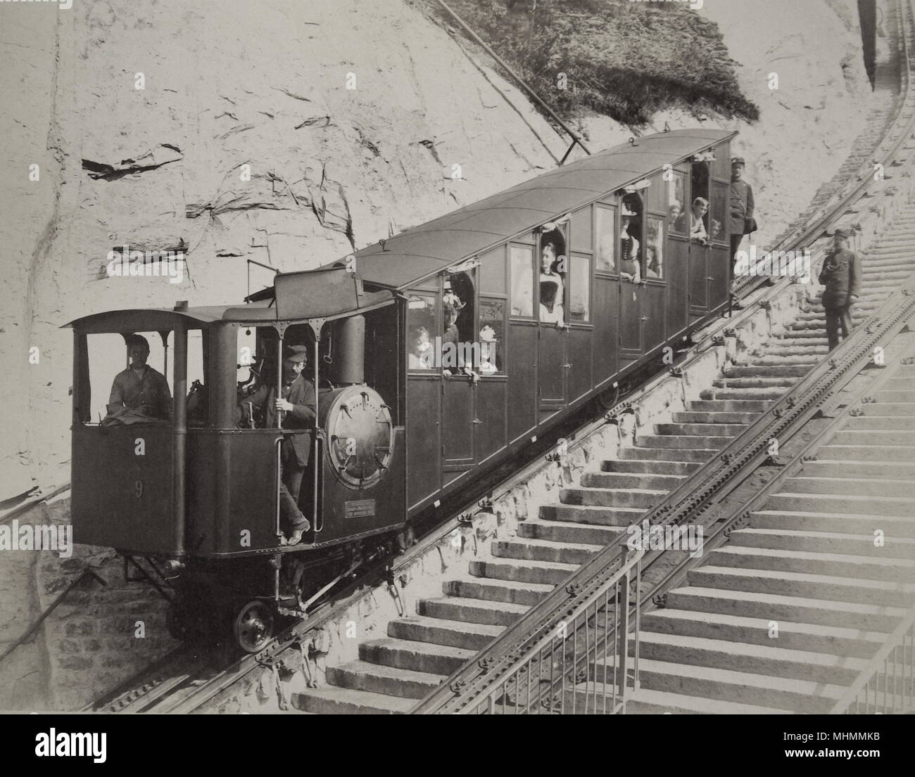 Un wagon de chemin de fer suisse à crémaillère et pignon à voie étroite, construit vers 1900, avec des conducteurs et des passagers, sur une piste en pente raide dans les Alpes, avec deux marches à côté. D'après les archives de Gloucester Coach and Wagon Works au Gloucester Record Office. Banque D'Images