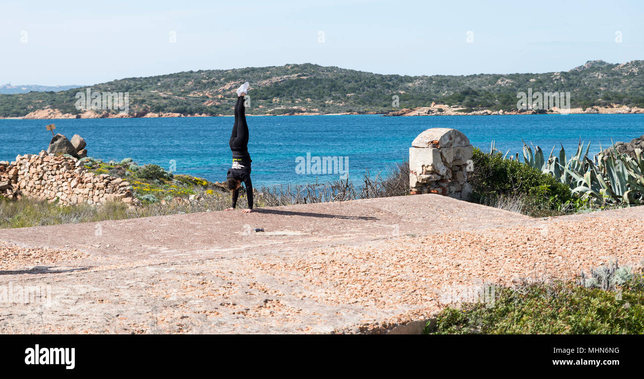 Boy doing handstand avec jambes écartées sur la route dans la partie ancienne de l'île de Maddalena Banque D'Images