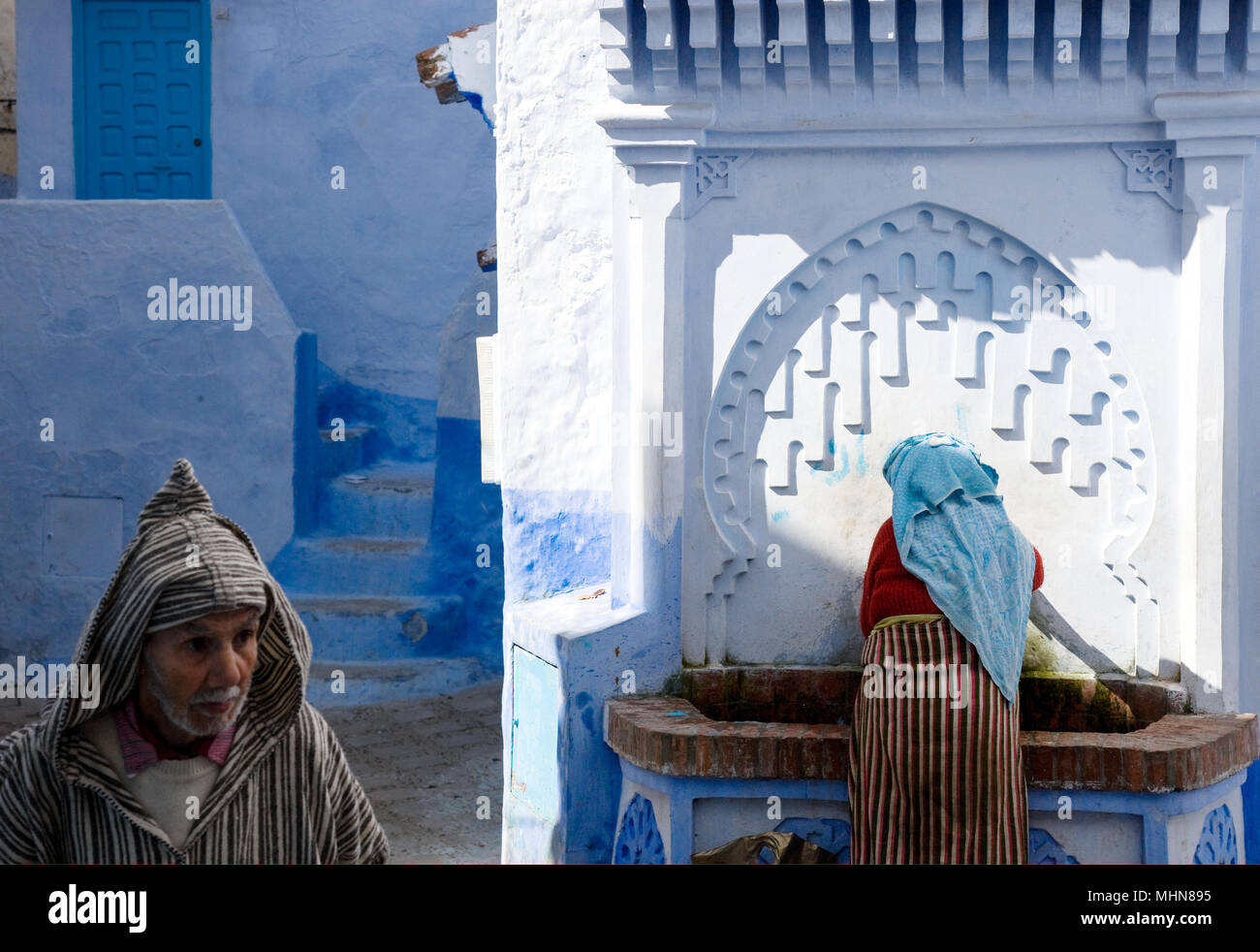 Chefchaouen, Maroc ; l'homme et la femme en costume traditionnel à la fontaine publique de la vieille ville. Banque D'Images