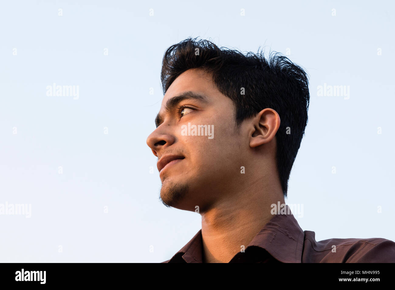 Dhaka, Bangladesh, le 24 février 2017 : Portrait of a smiling young man du Bangladesh avec une chemise brune dans la lumière du soir pris d'en bas Banque D'Images