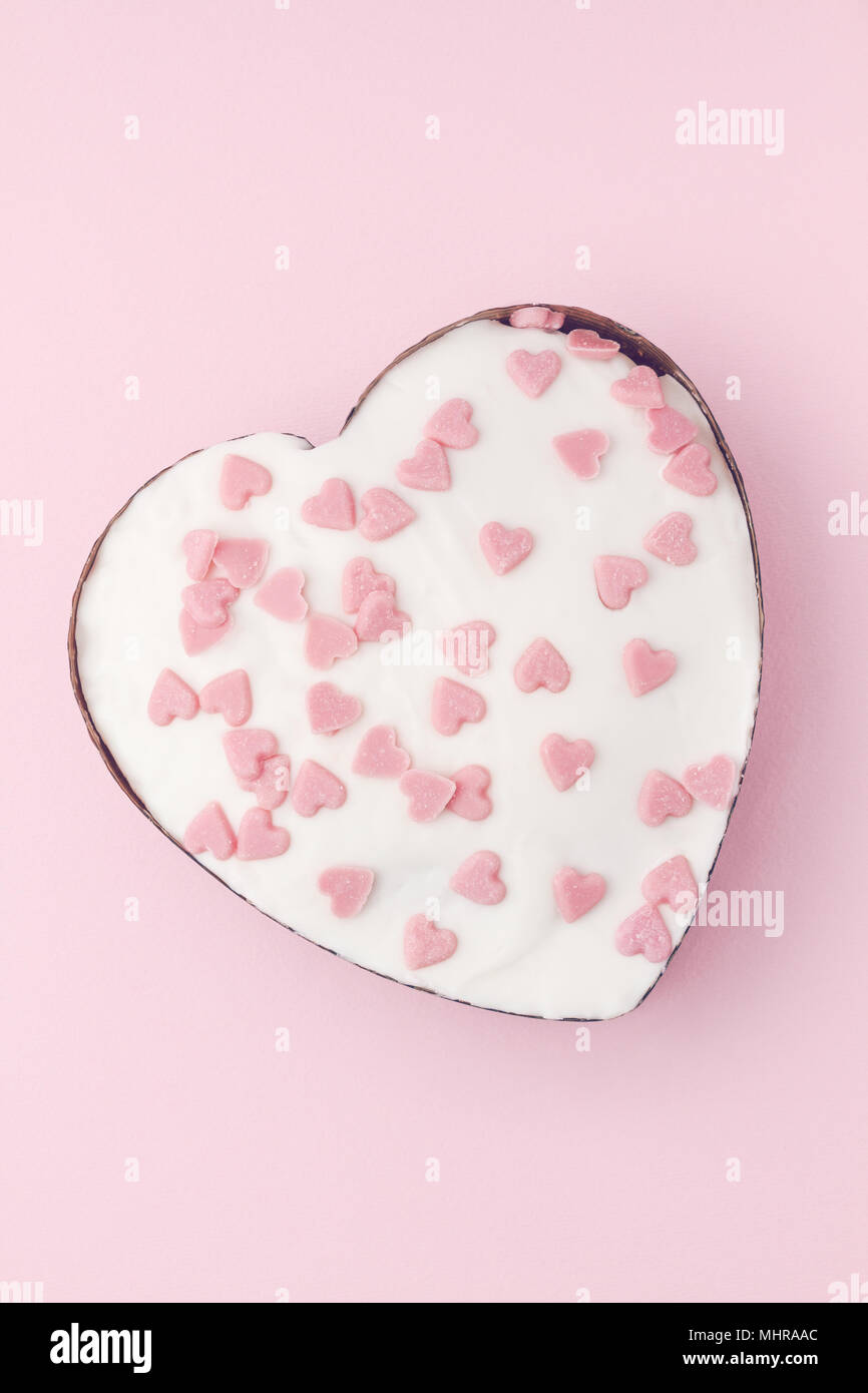 Muffin en forme de coeur blanc décoré avec des coeurs de sucre rose sur fond rose. Vertical image. Banque D'Images