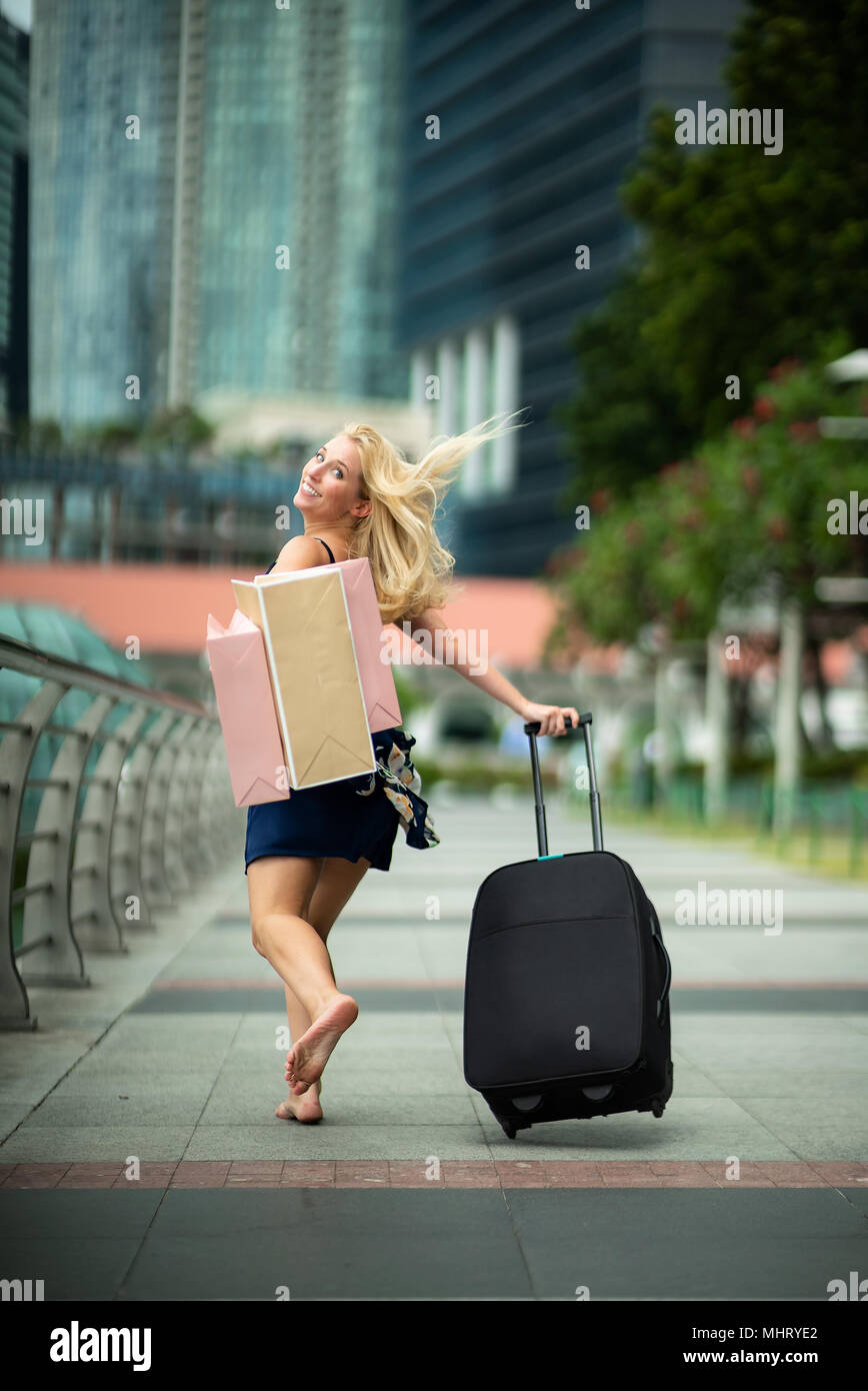 Happy Traveler après shopping... Heureux belle femme portant robe bleue occasionnels avec des fleurs, la tenue noire et les sacs dans le stree Banque D'Images