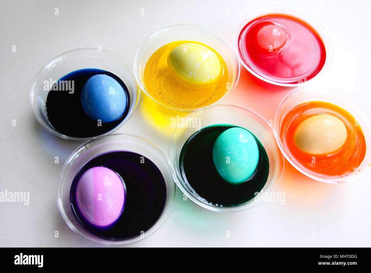 Une image lumineuse et colorée des oeufs fait teindre pour Pâques. Des colorants dans des tasses avec de l'oeuf dans chacun, différentes couleurs, isolé sur blanc. Banque D'Images