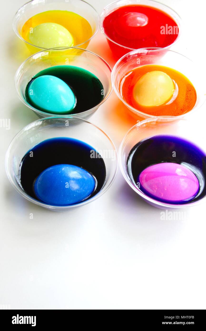 Une image lumineuse et colorée des oeufs fait teindre pour Pâques. Des colorants dans des tasses avec de l'oeuf dans chacun, différentes couleurs, isolé sur blanc. Banque D'Images