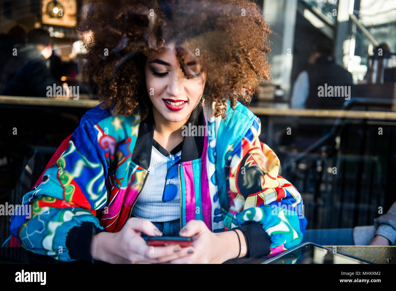 Jeune fille assise dans un bar, à l'aide de smartphone, voir à travers la vitre, London, England, UK Banque D'Images