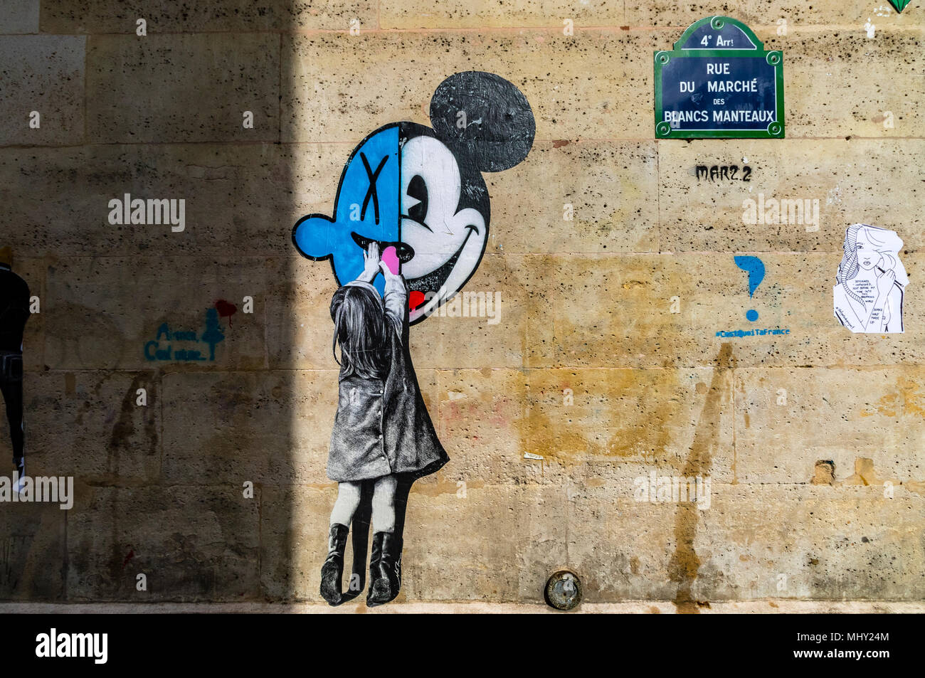 Une petite fille atteint jusqu'à toucher la souris de Mickey, une peinture de rue sur un mur de la rue du marché des Blancs Manteaux, Paris, France Banque D'Images