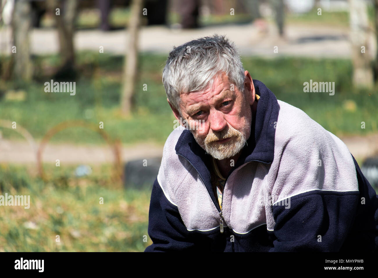 Barbu aux cheveux gris vieil homme assis sur un banc et attend Banque D'Images