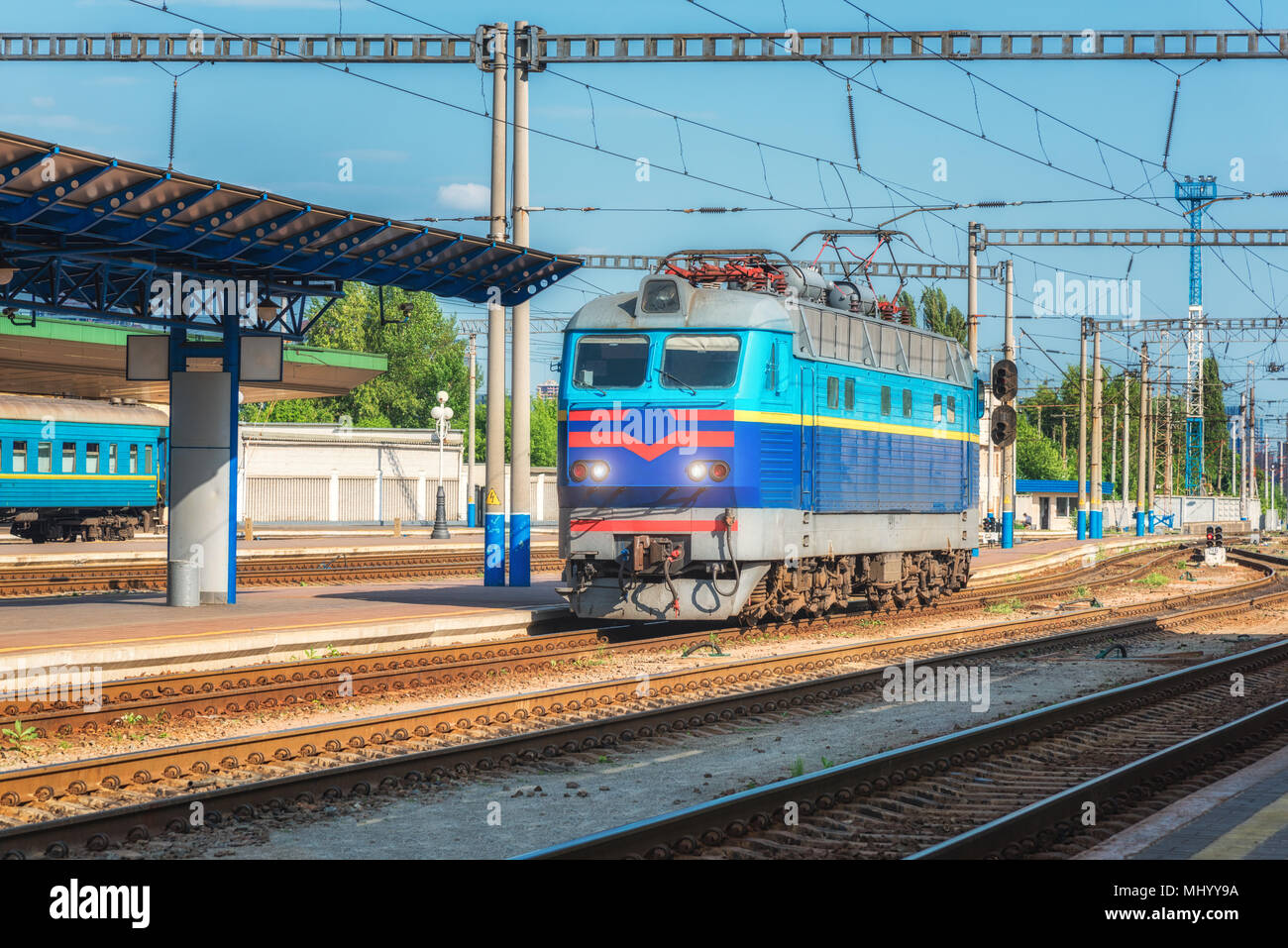 Le train bleu sur la gare au coucher du soleil en Ukraine. Paysage industriel avec de vieux bâtiments, des locomotives, des rails et ciel bleu avec des nuages. T Banque D'Images