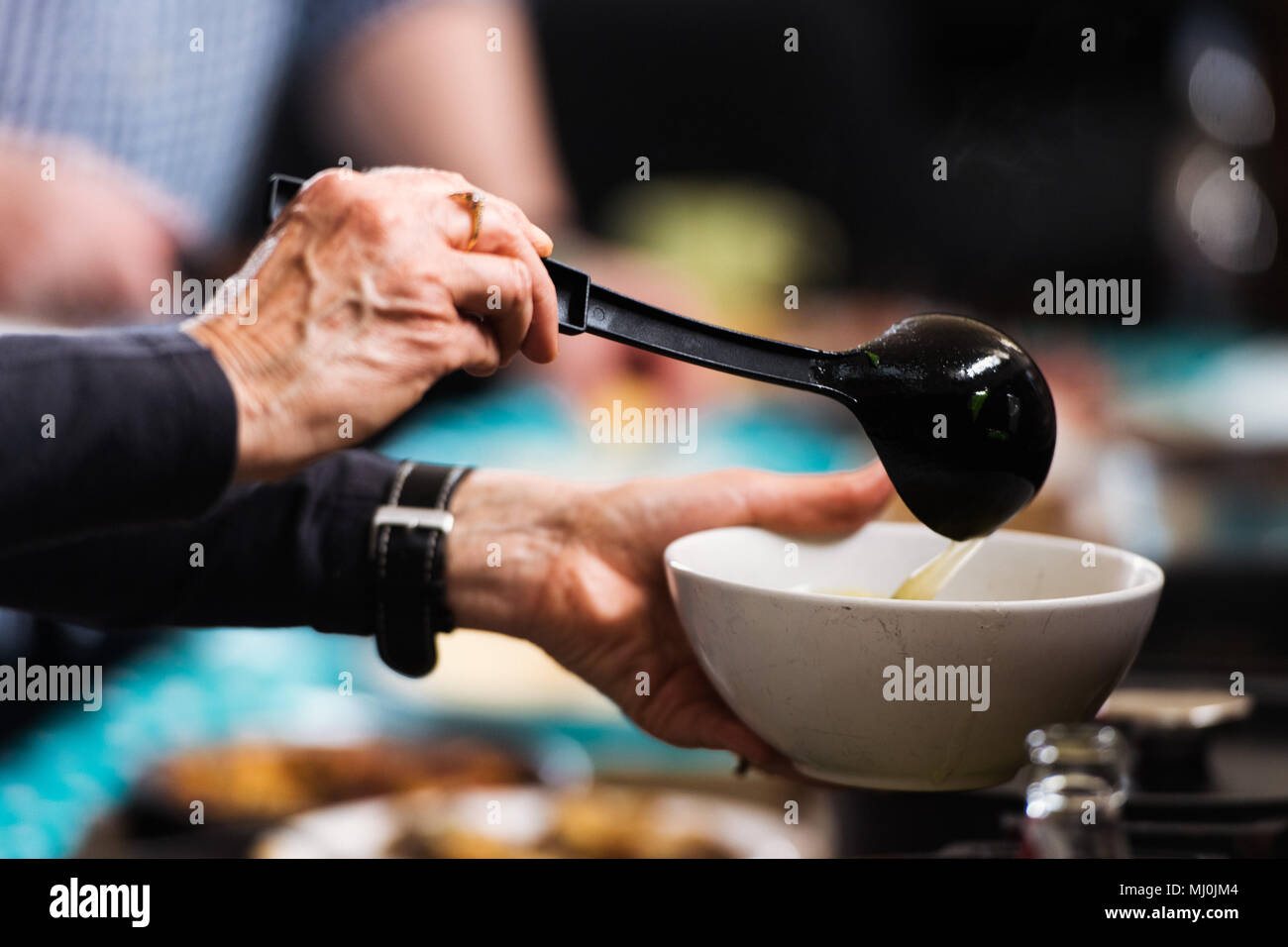 Mains louche soupe dans un bol Banque D'Images